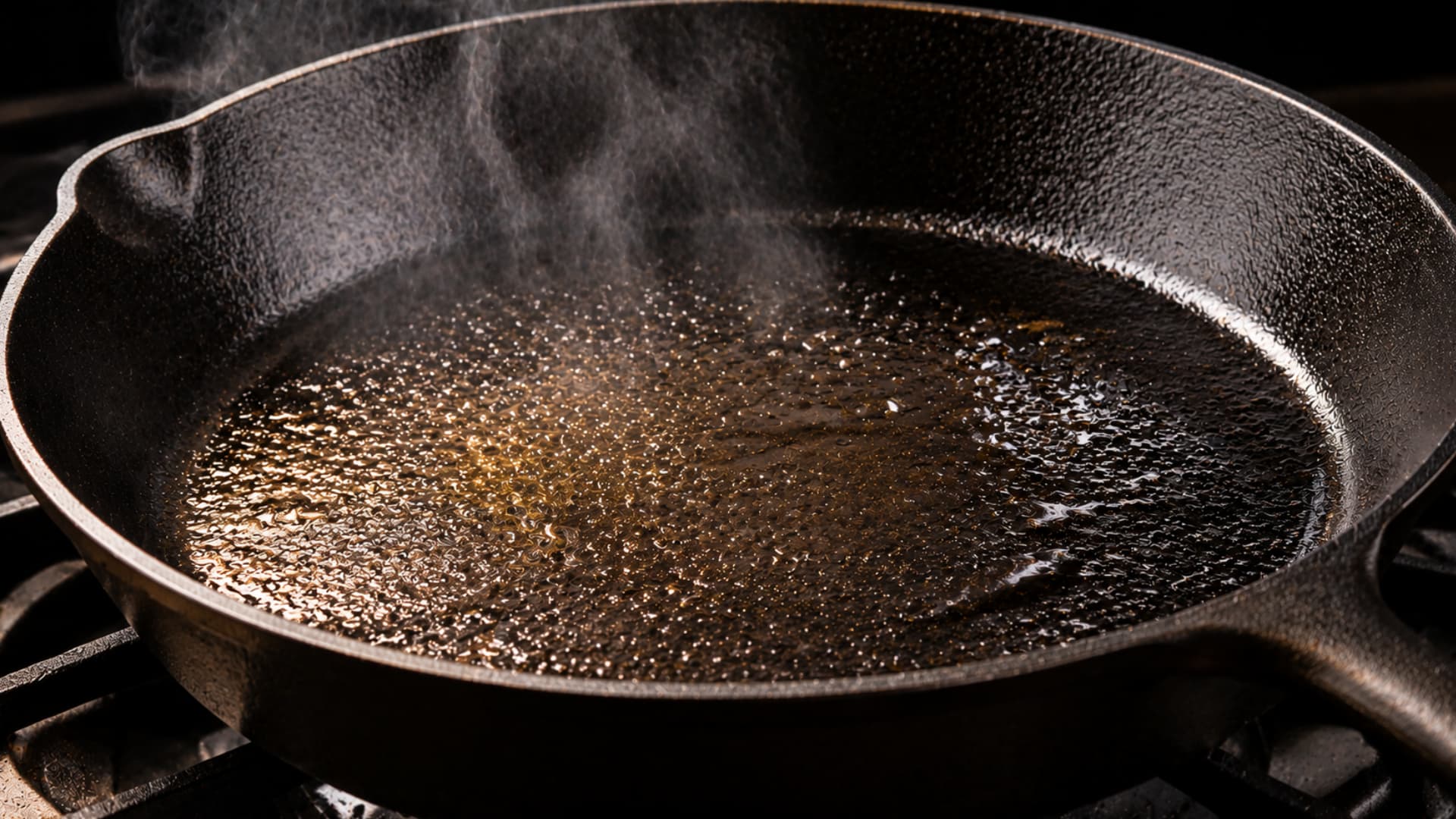 hot cast iron skillet with oil heating and steam rising from surface close up cooking shot dramatic lighting rustic kitchen scene