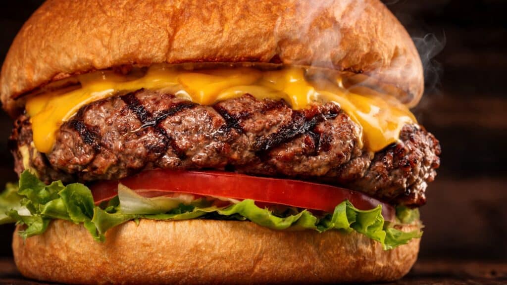 juicy beef burger with grilled patty melted cheese toasted bun lettuce and tomato on rustic wooden table with steam rising