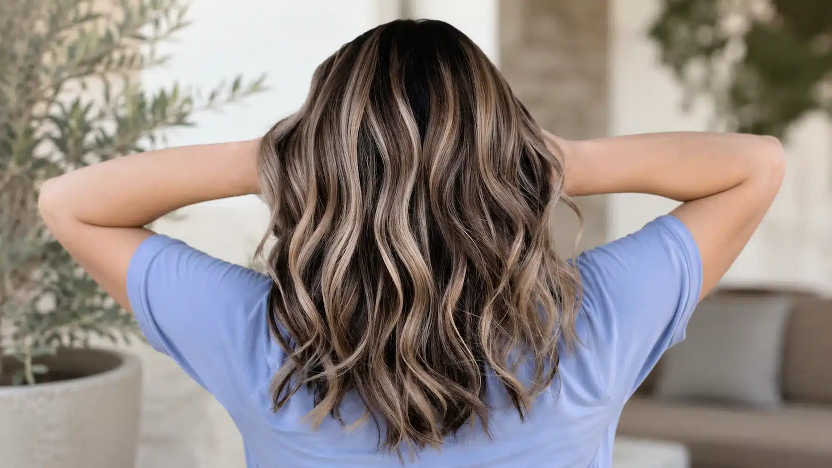 back view of wavy brunette hair with blonde balayage highlights in a soft patio setting