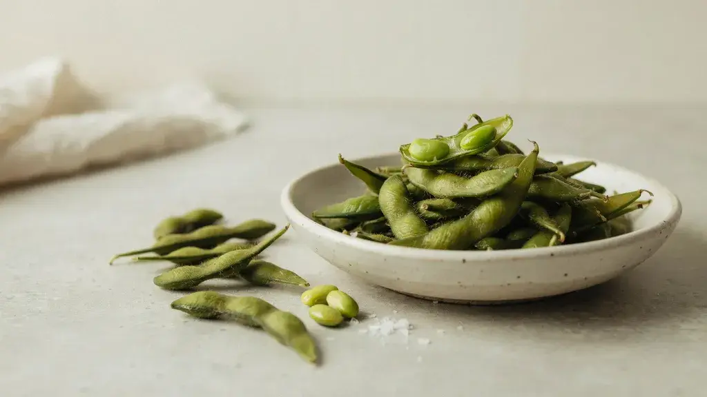 Fresh green edamame pods in ceramic bowl with loose beans and opened pod showing natural textures and vibrant color