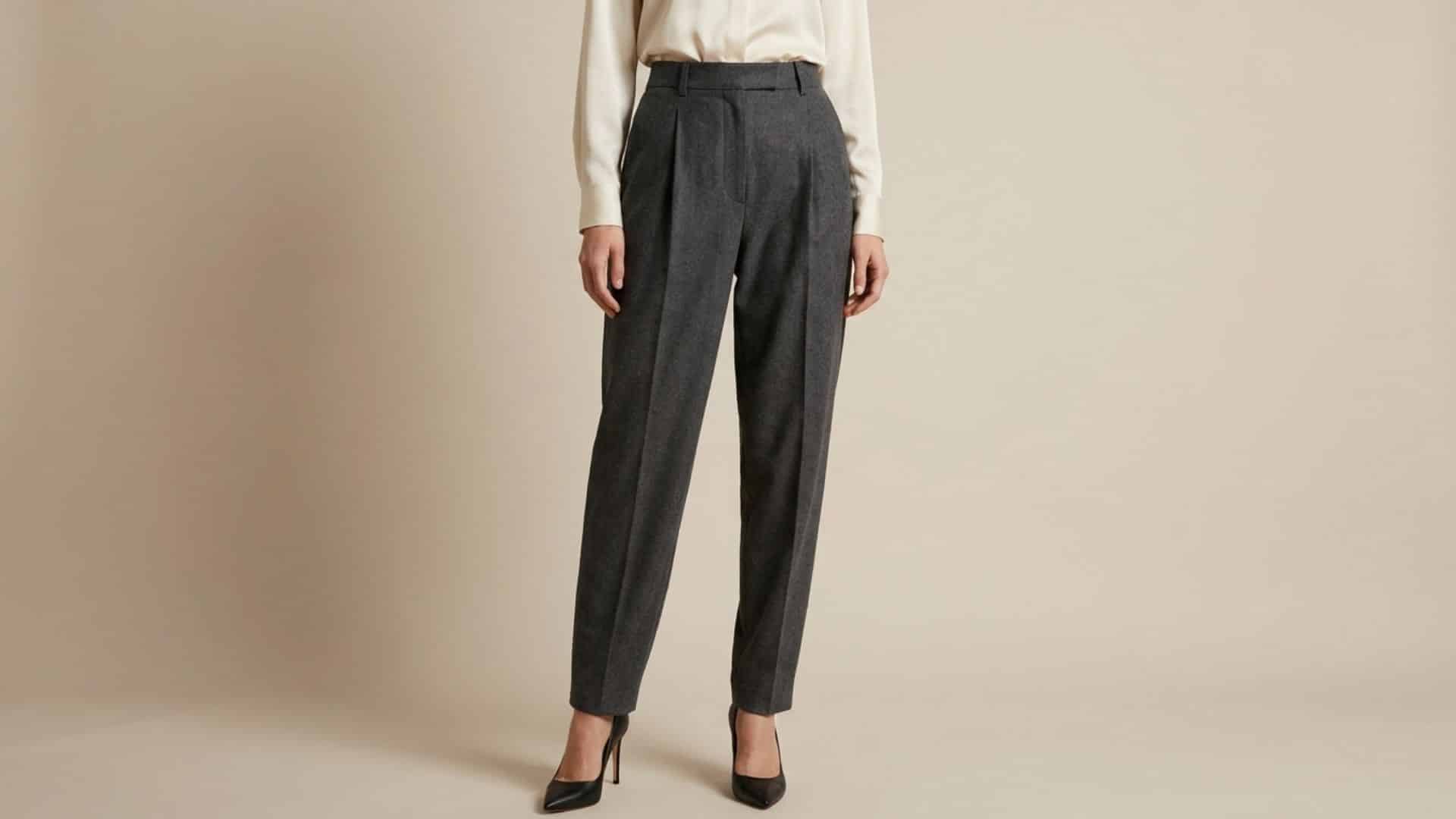 Woman wearing tailored pleated trousers with structured front folds, premium fabric texture, and sophisticated fit against a neutral background
