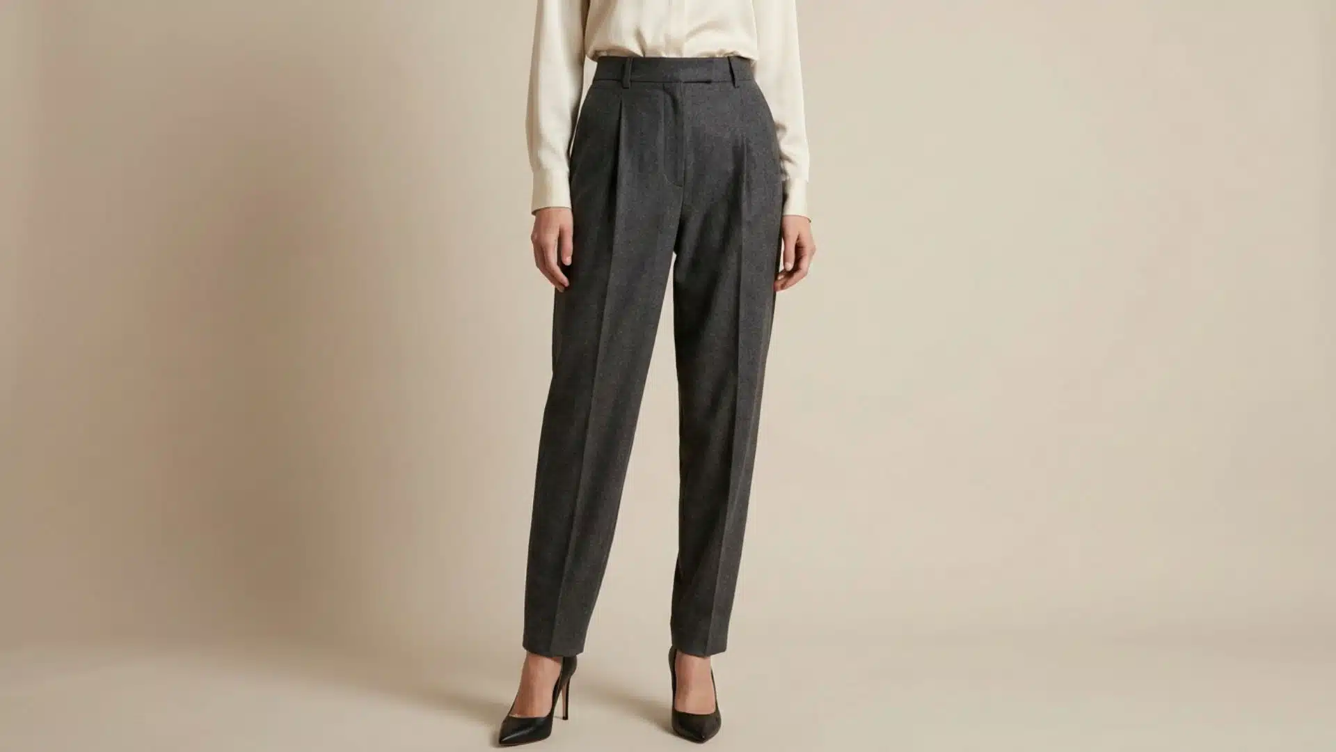 Woman wearing tailored pleated trousers with structured front folds, premium fabric texture, and sophisticated fit against a neutral background