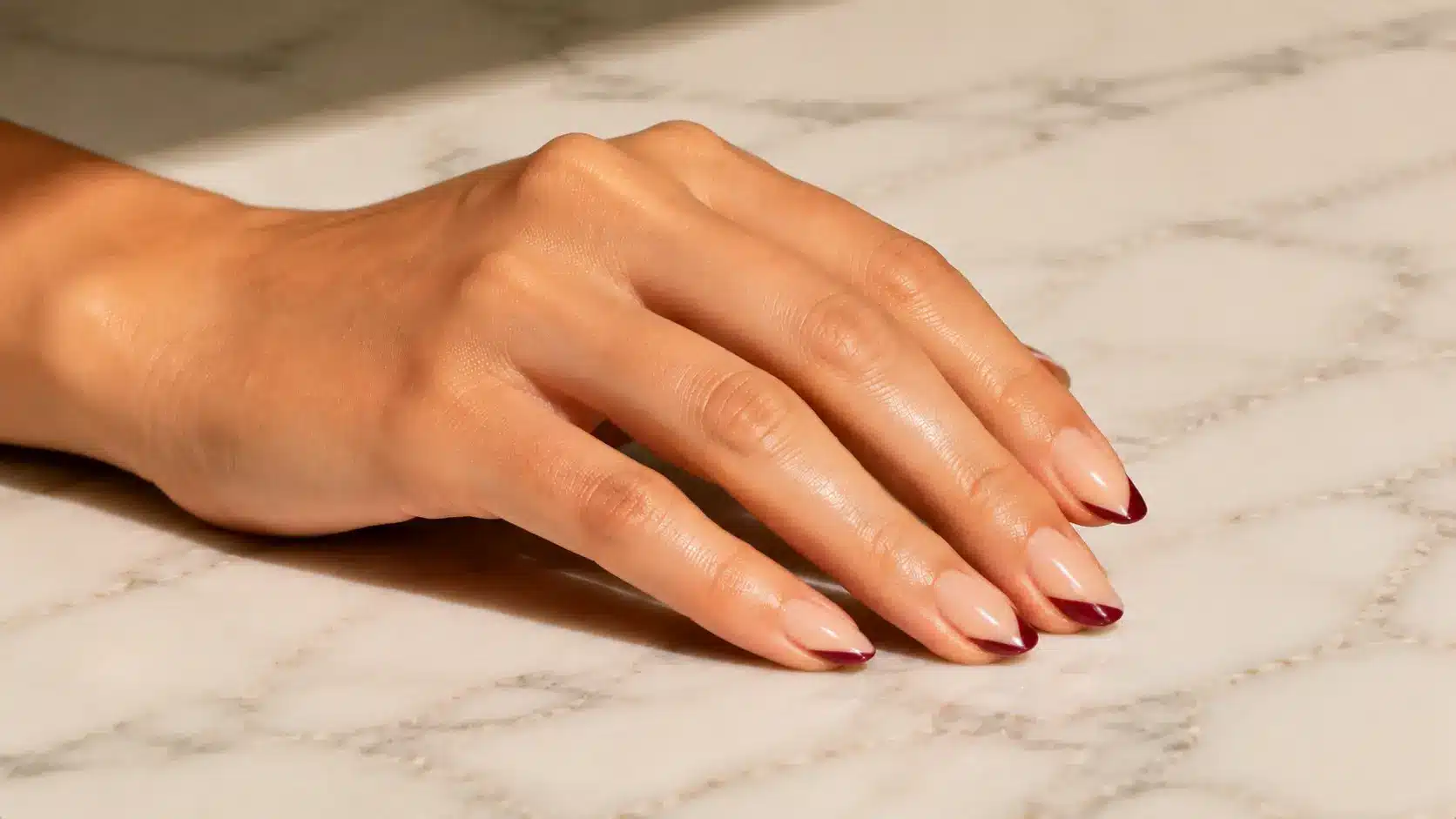 Diagonal French nail design featuring glossy nude nails with angled burgundy tips for a modern simple nail art look