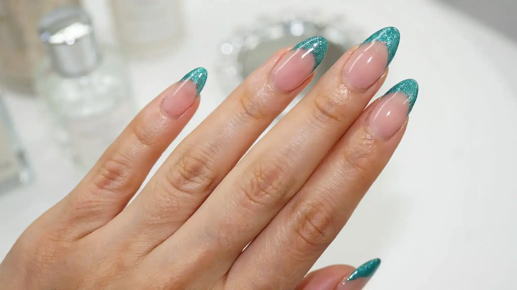 Nude nails with teal glitter French tips on a hand.