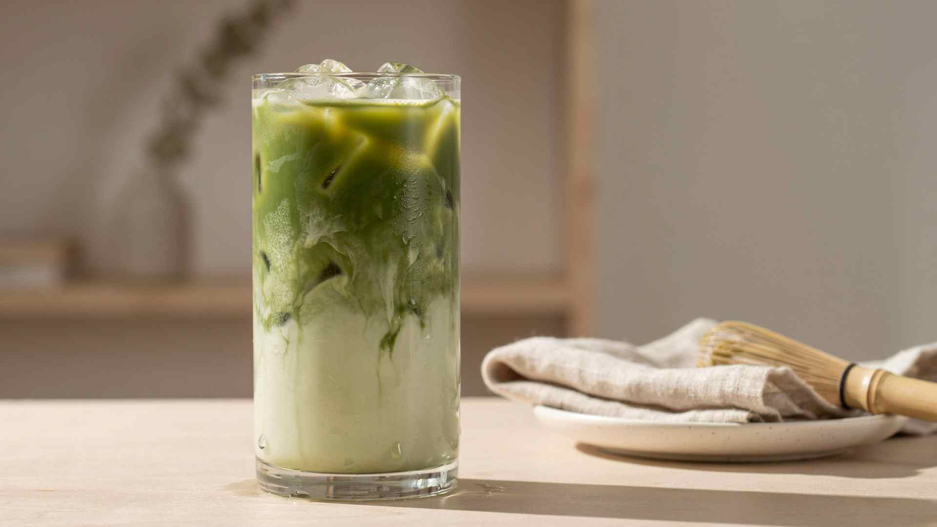 Iced matcha in a glass with ice and a bamboo whisk