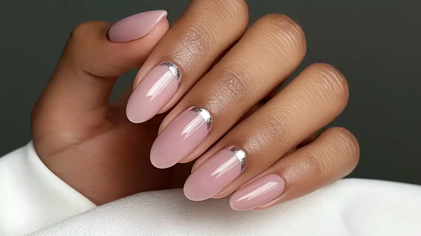 Glossy pink almond nails with a silver glitter reverse French tip design.