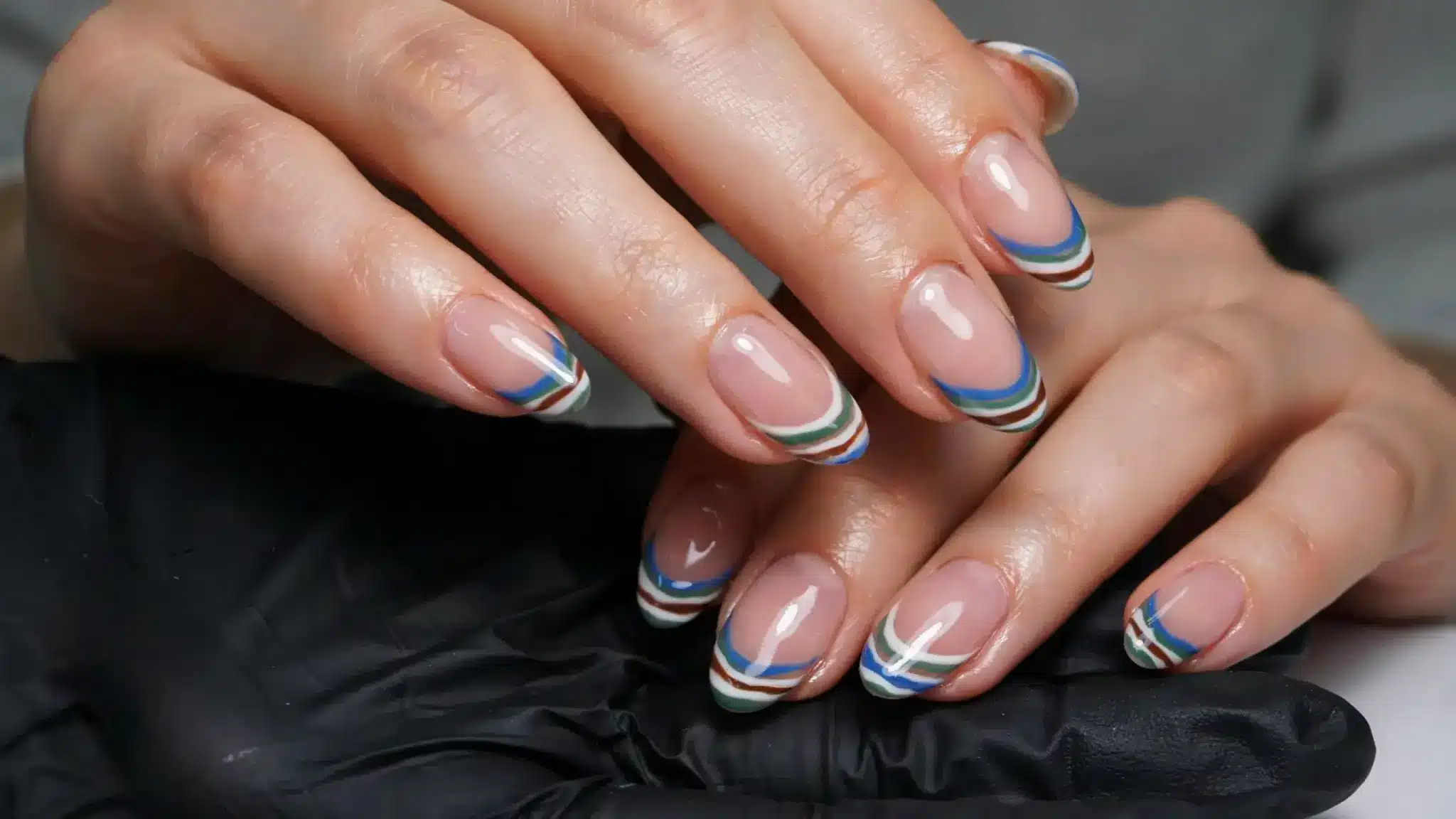 Nude glossy nails with blue, green, and white curved French tip designs.