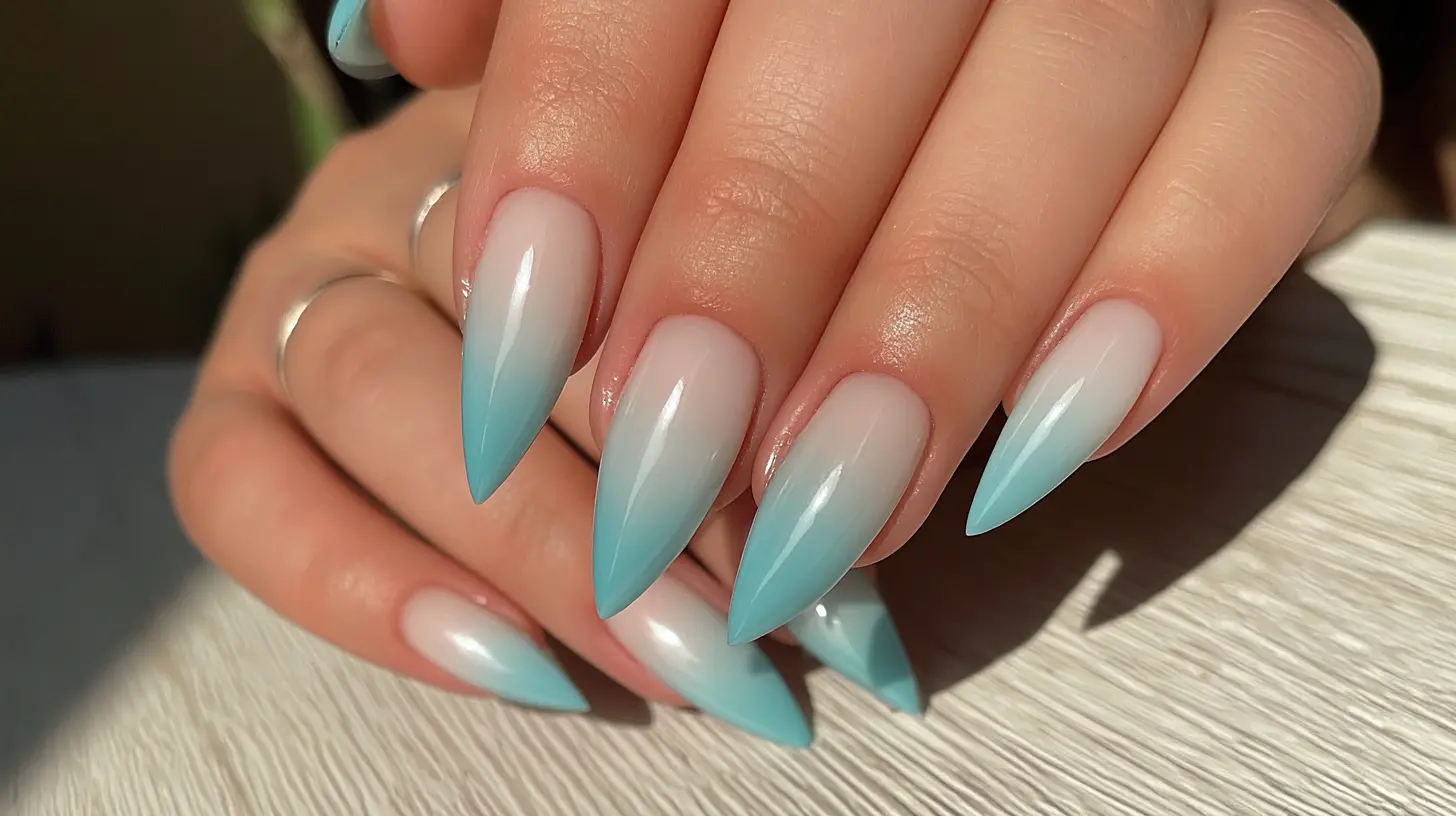 Close-up of almond-shaped nails featuring a glossy ombre design transitioning from nude to light blue.