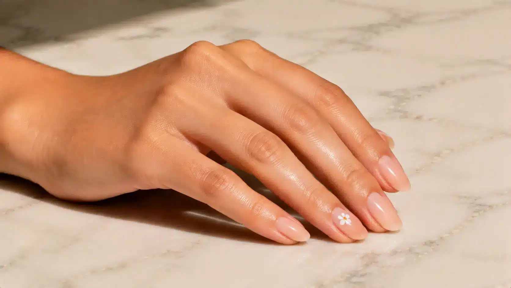 Single flower accent nail design featuring glossy nude nails with a delicate white flower for a simple nail art look