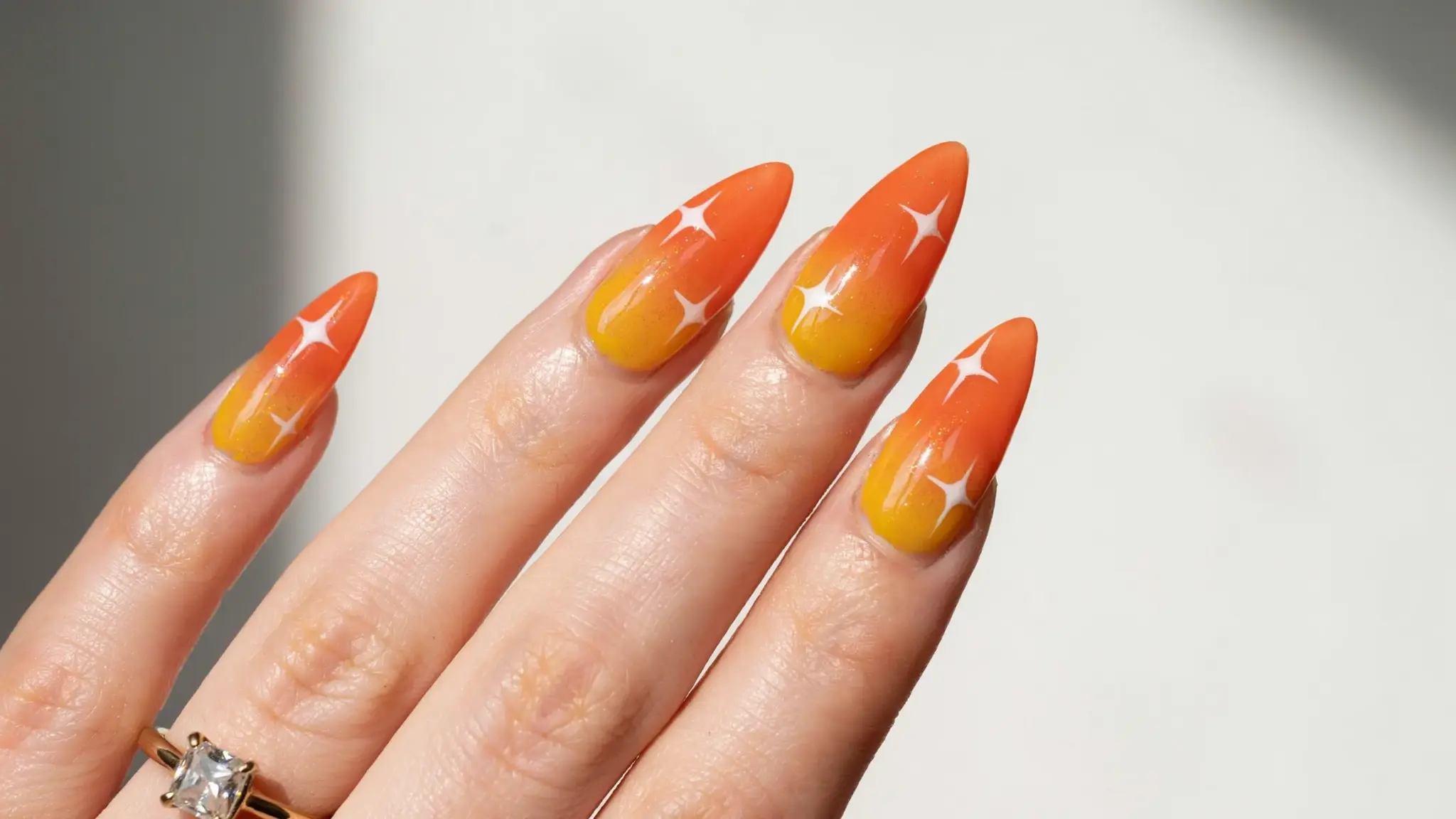 Orange and yellow sunset gradient nail art with glossy finish on a hand.