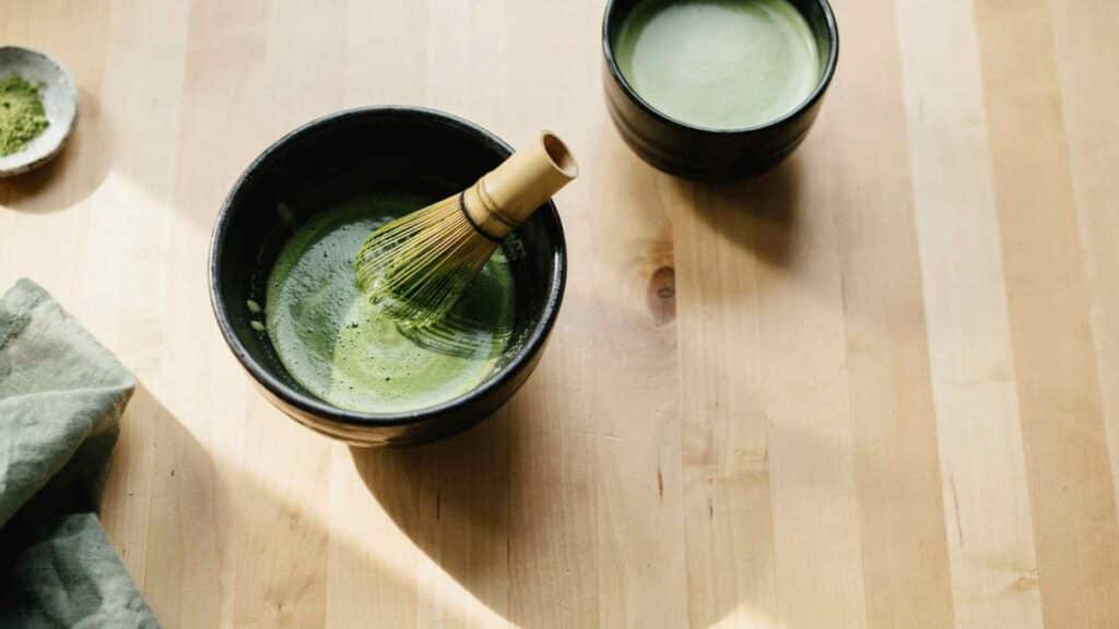 Matcha being whisked in a ceramic bowl beside a matcha drink