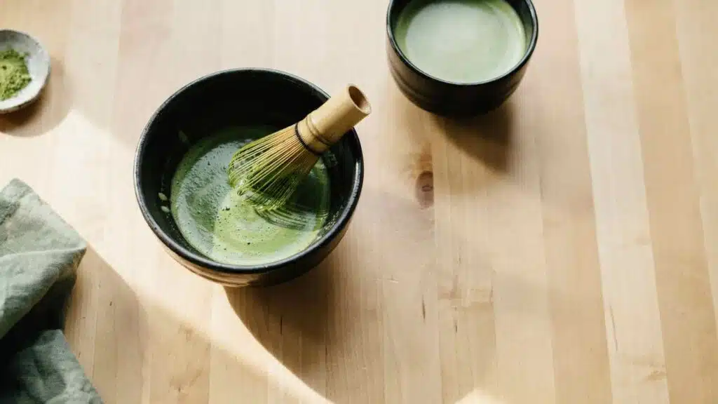 Matcha being whisked in a ceramic bowl beside a matcha drink